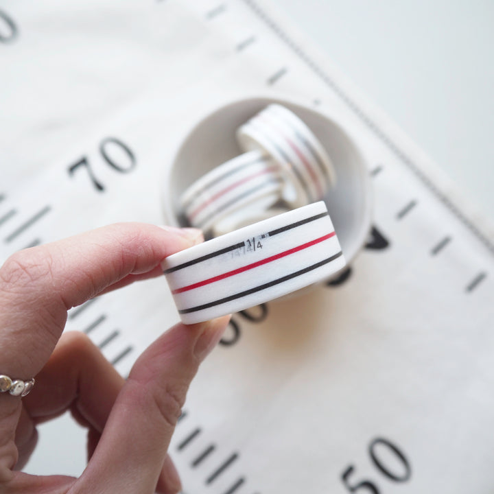 Hand holding a roll of washi tape with red and blue stripes against a blurred background
