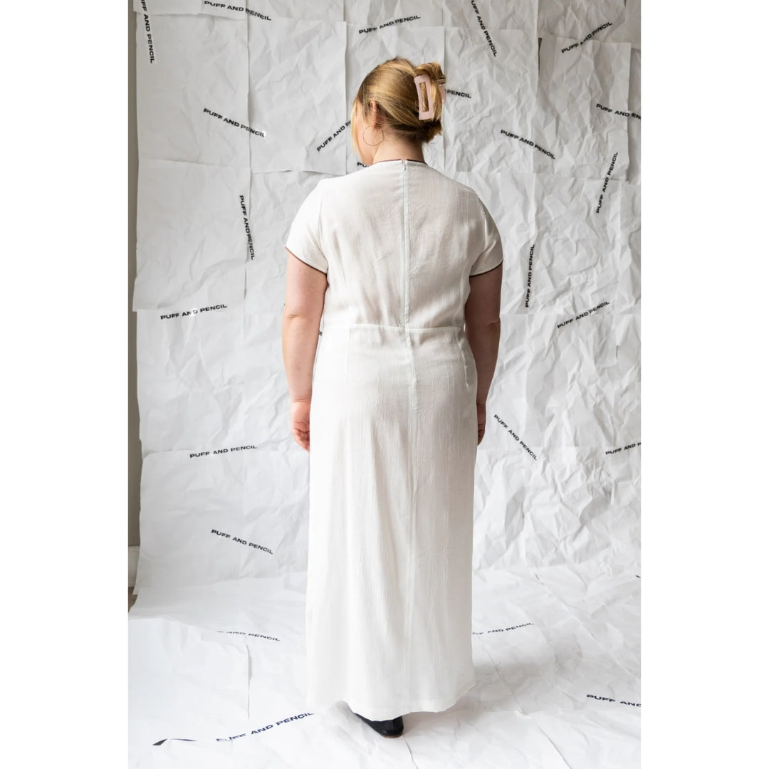 Person wearing a white dress standing against a textured white background
