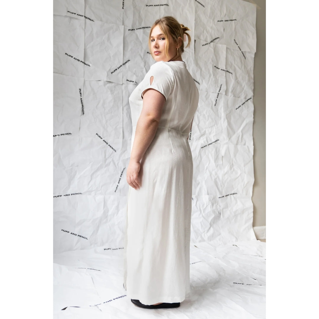 Woman wearing a white dress against a textured white wall.