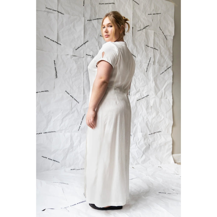 Woman wearing a white dress against a textured white wall.