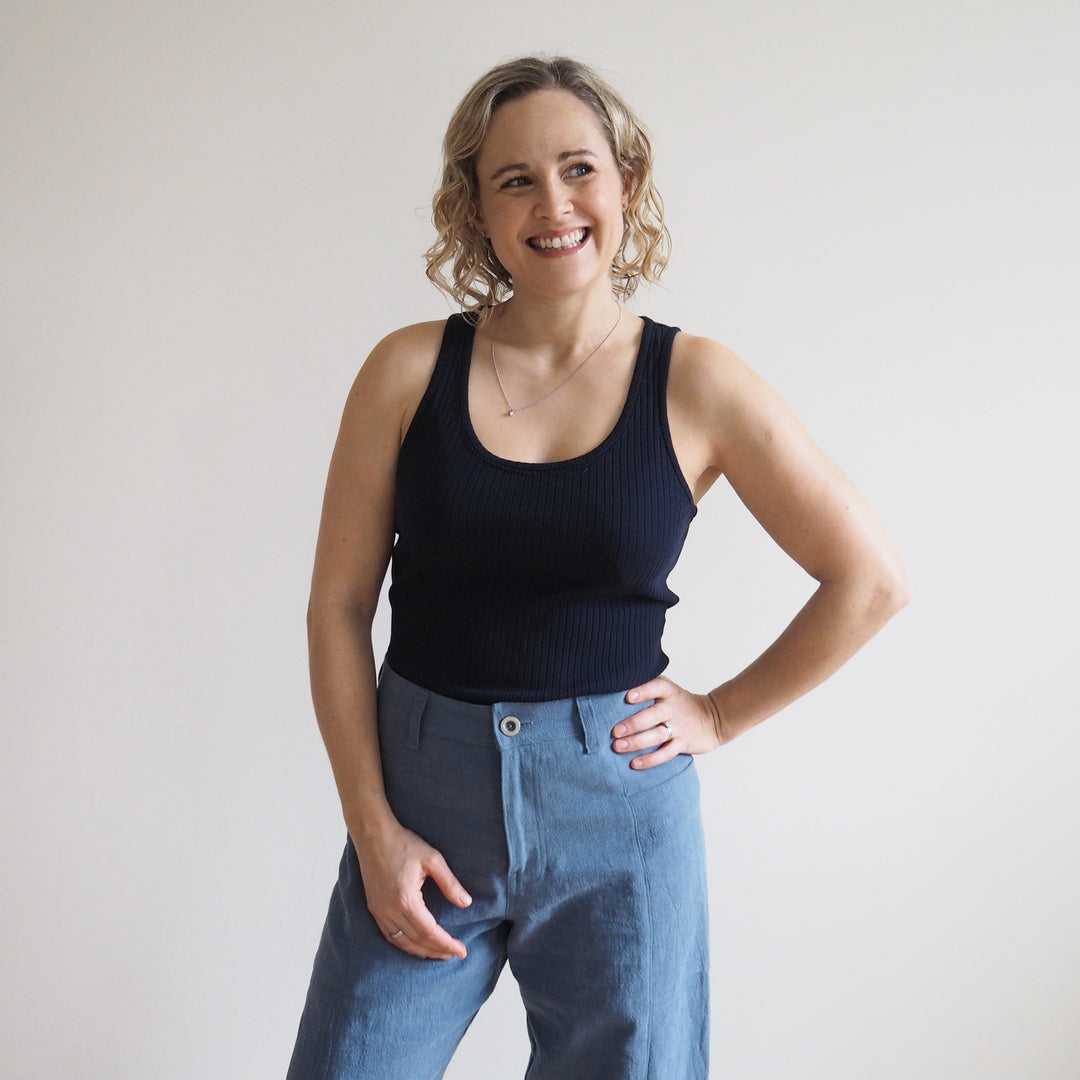 Woman wearing a black tank top and blue jeans against a plain background