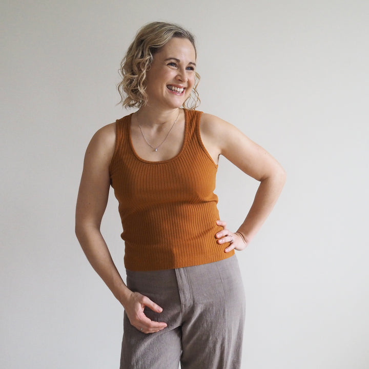 Woman wearing a brown tank top and gray pants against a plain background
