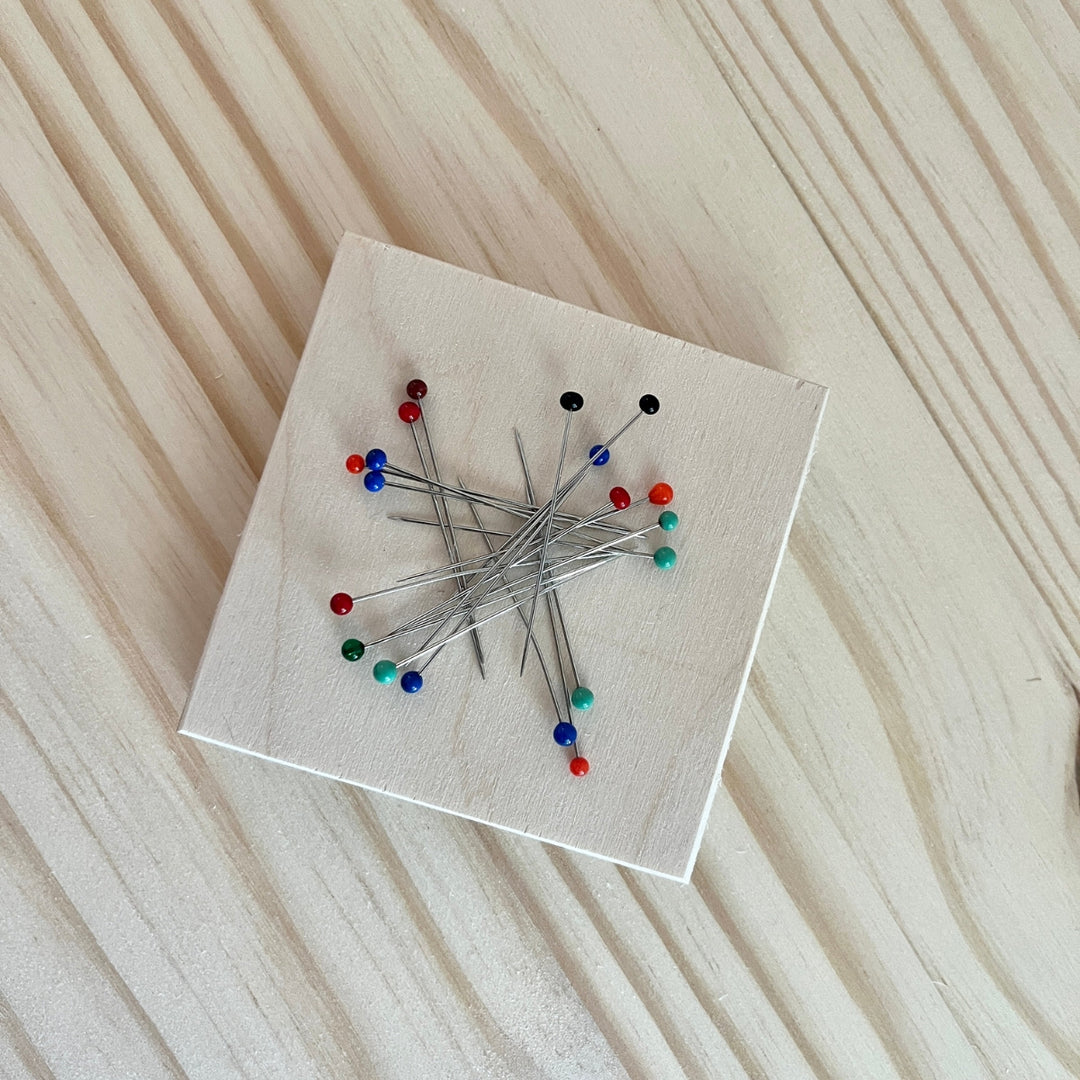 Collection of pins on a square white wooden tool with a wooden background