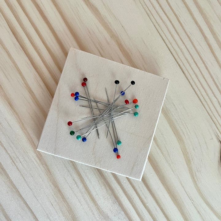 Collection of pins on a square white wooden tool with a wooden background