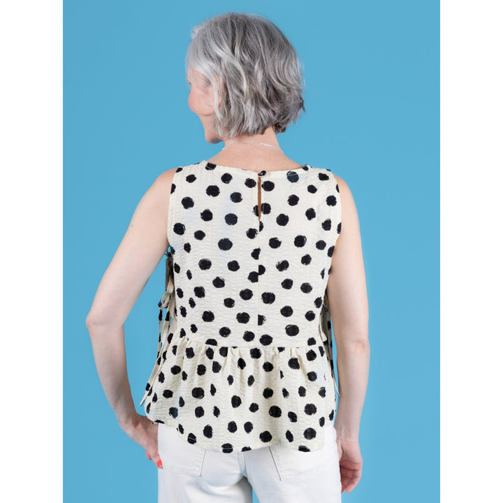 Woman wearing a sleeveless polka dot top against a blue background
