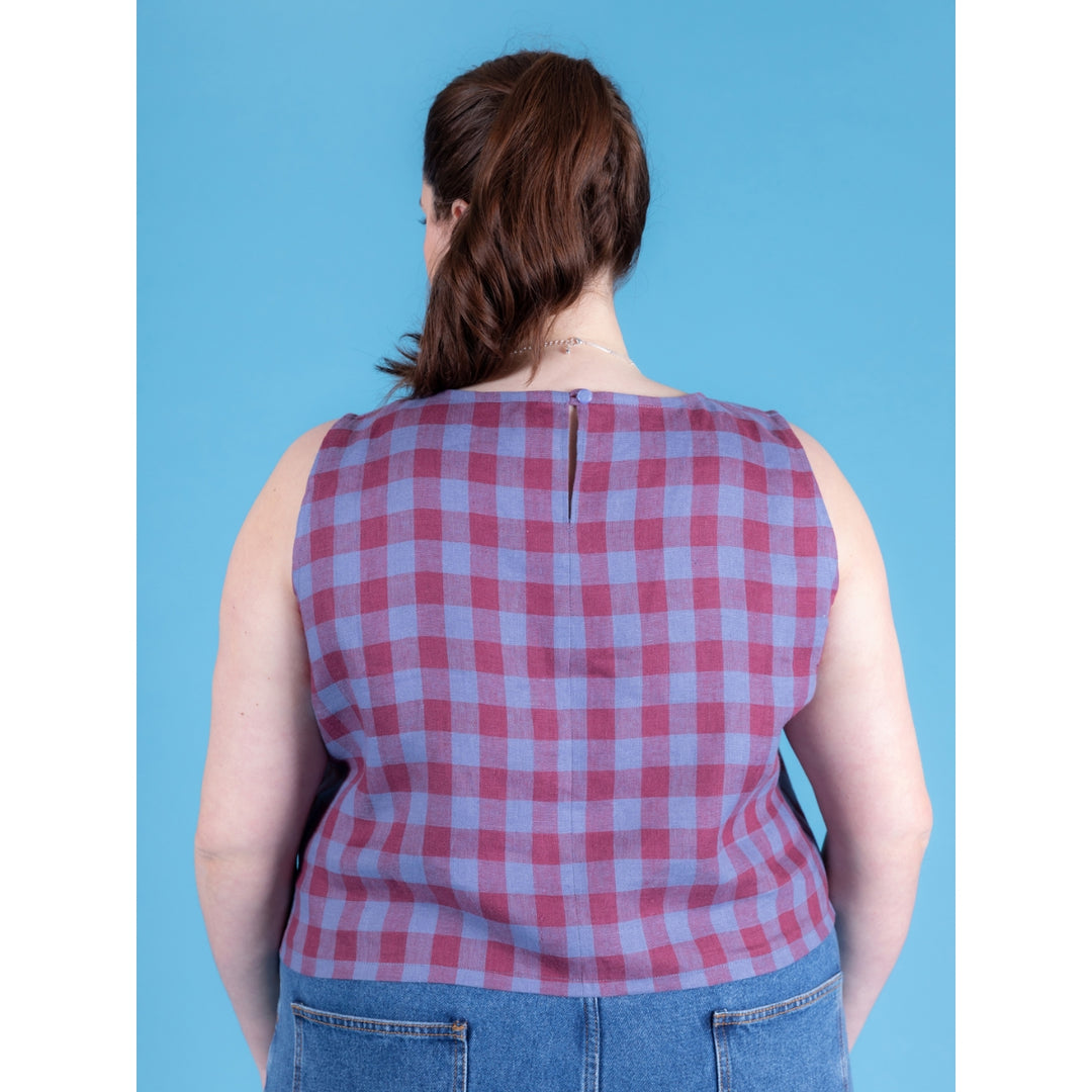 Person wearing a red and blue checkered sleeveless top against a blue background