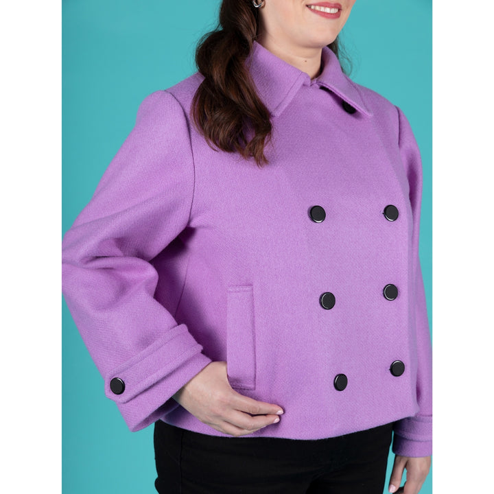 A woman wearing a lavender-purple double-breasted coat with black buttons, shown from the chin down against a solid teal background.