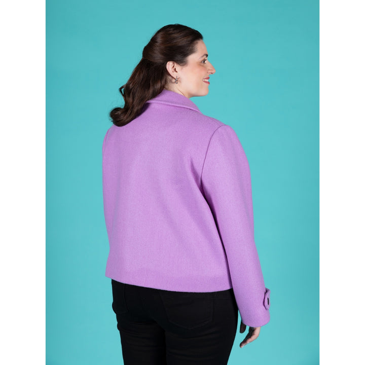 A woman wearing a lavender purple cropped jacket, shown from the back and side profile against a solid turquoise background.