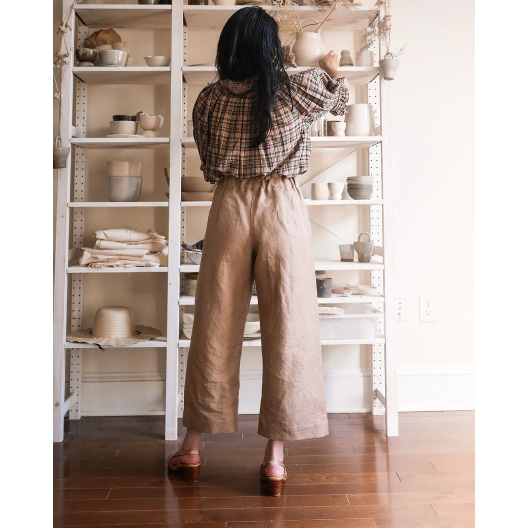 Person in plaid shirt and beige pants standing in front of a white shelving unit with various items.