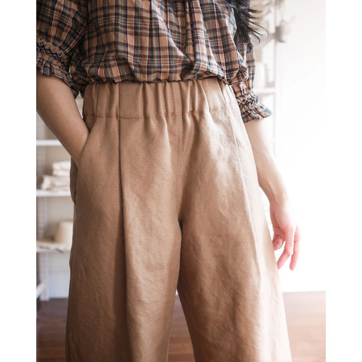 Person wearing a plaid shirt and beige pants in a softly lit room.