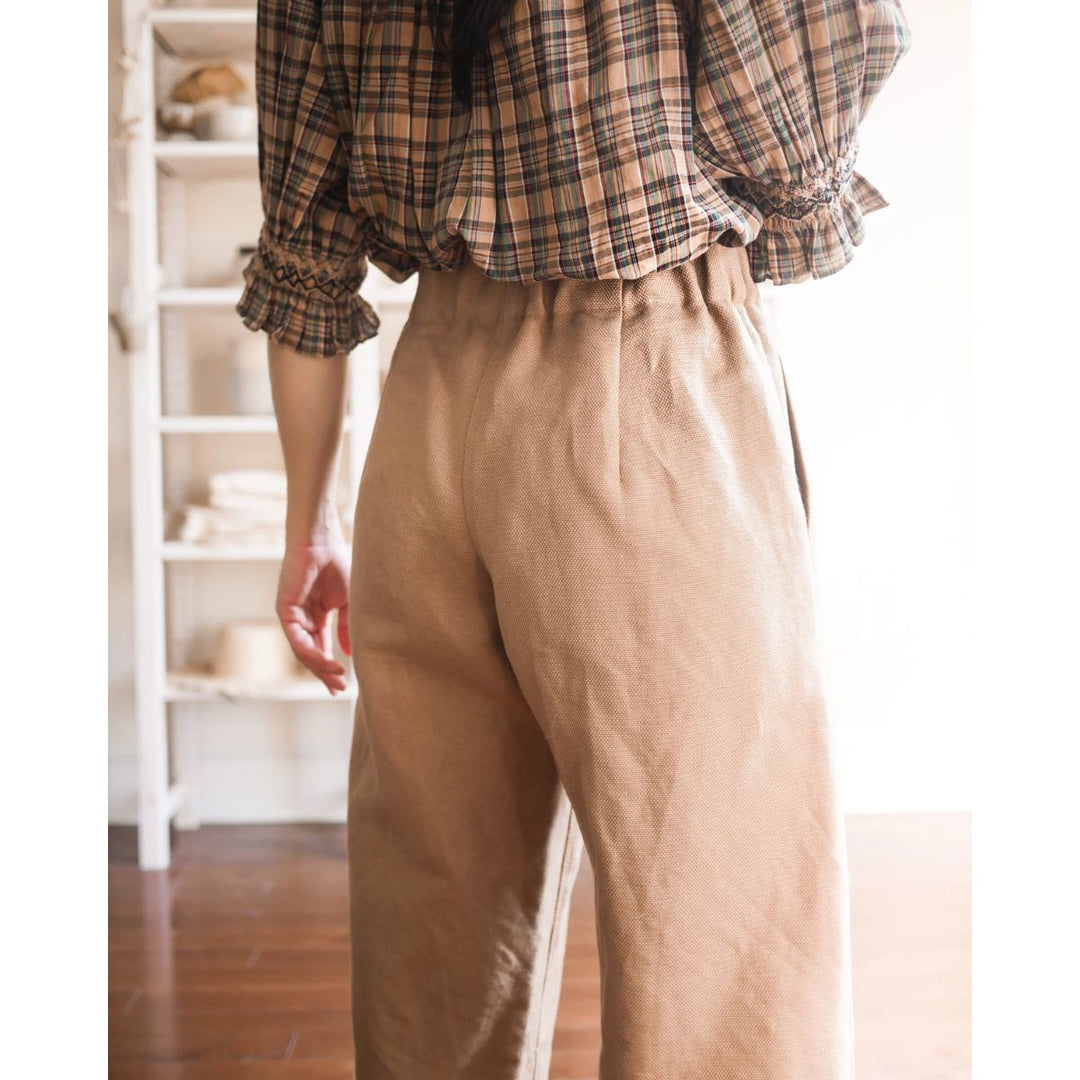 Person wearing a plaid shirt and beige pants in a softly lit room.