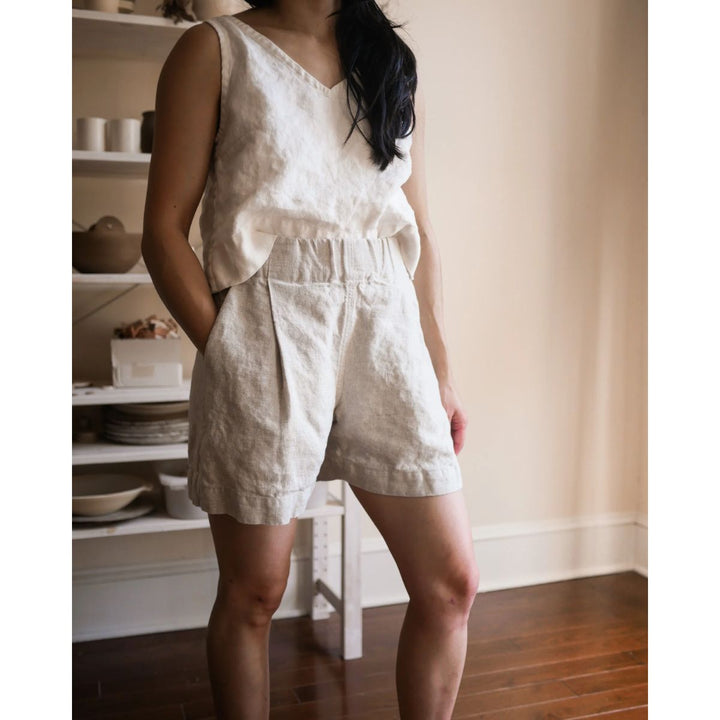 Person wearing a white sleeveless top and shorts set in a room with shelves in the background.