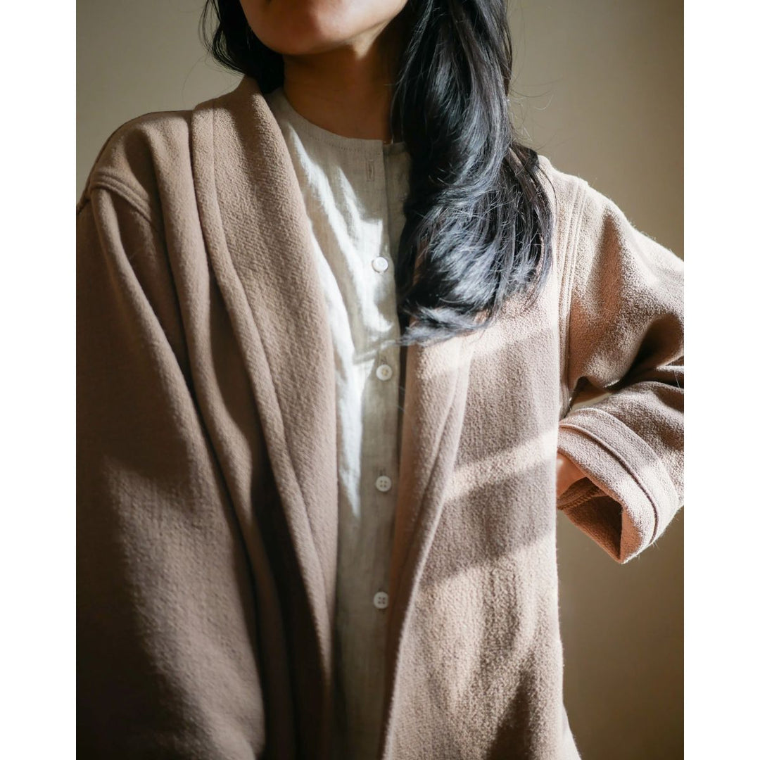 Person wearing a beige cardigan over a light shirt with a neutral background
