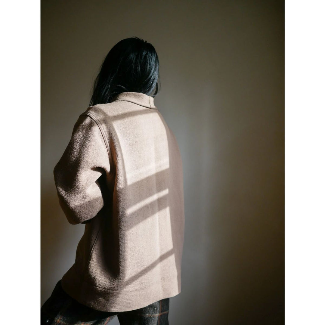 Person wearing a beige coat with a shadow pattern on a plain background