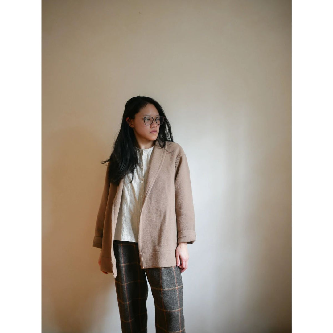 Person wearing a beige coat and plaid pants against a plain background