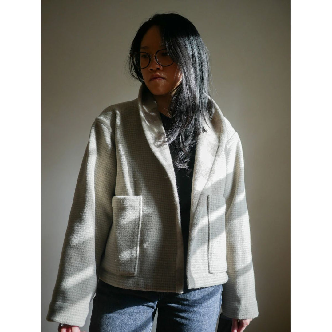 Person wearing a light gray jacket with a plain background