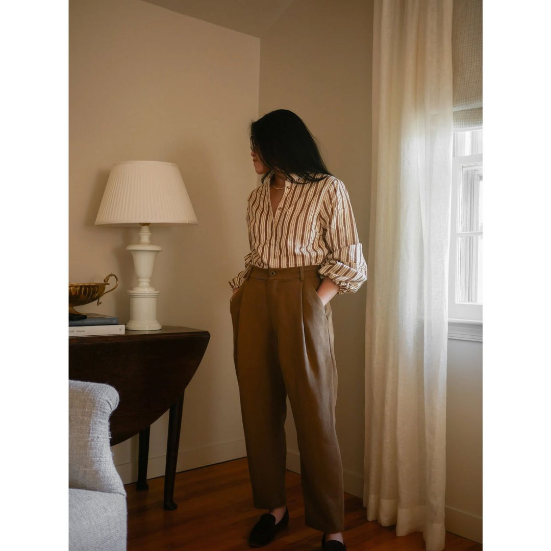 Woman standing in a room with a lamp and window curtains.