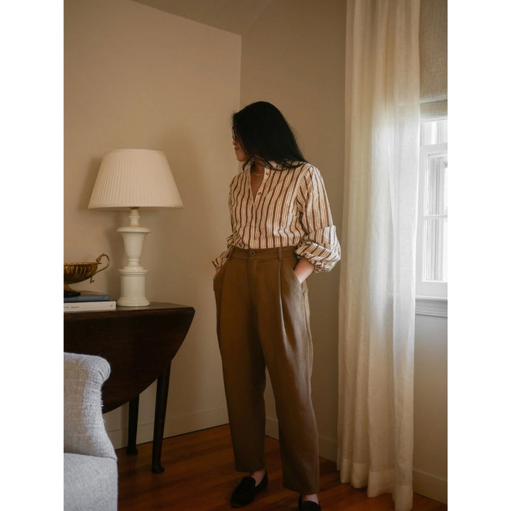 Woman standing in a room with a lamp and window curtains.