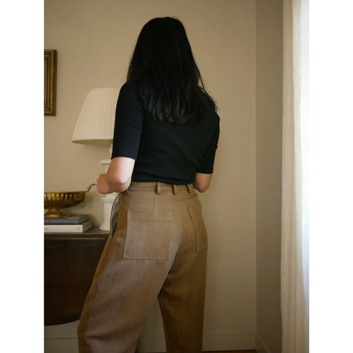 Person wearing a black shirt and beige pants standing in a room with a lamp and decor items.