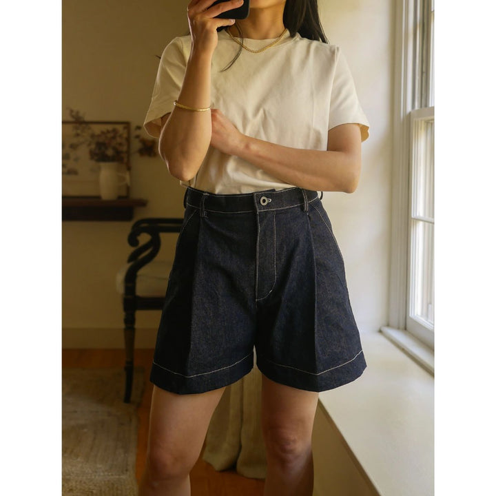 Person wearing a white t-shirt and dark denim shorts in a room with a window.