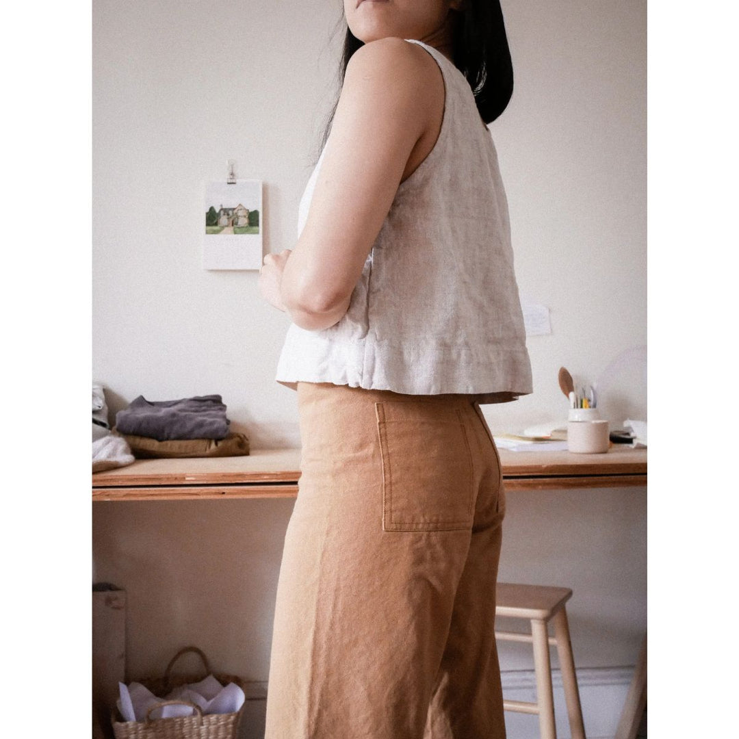 Person wearing a light-colored sleeveless top and brown pants in a home setting.