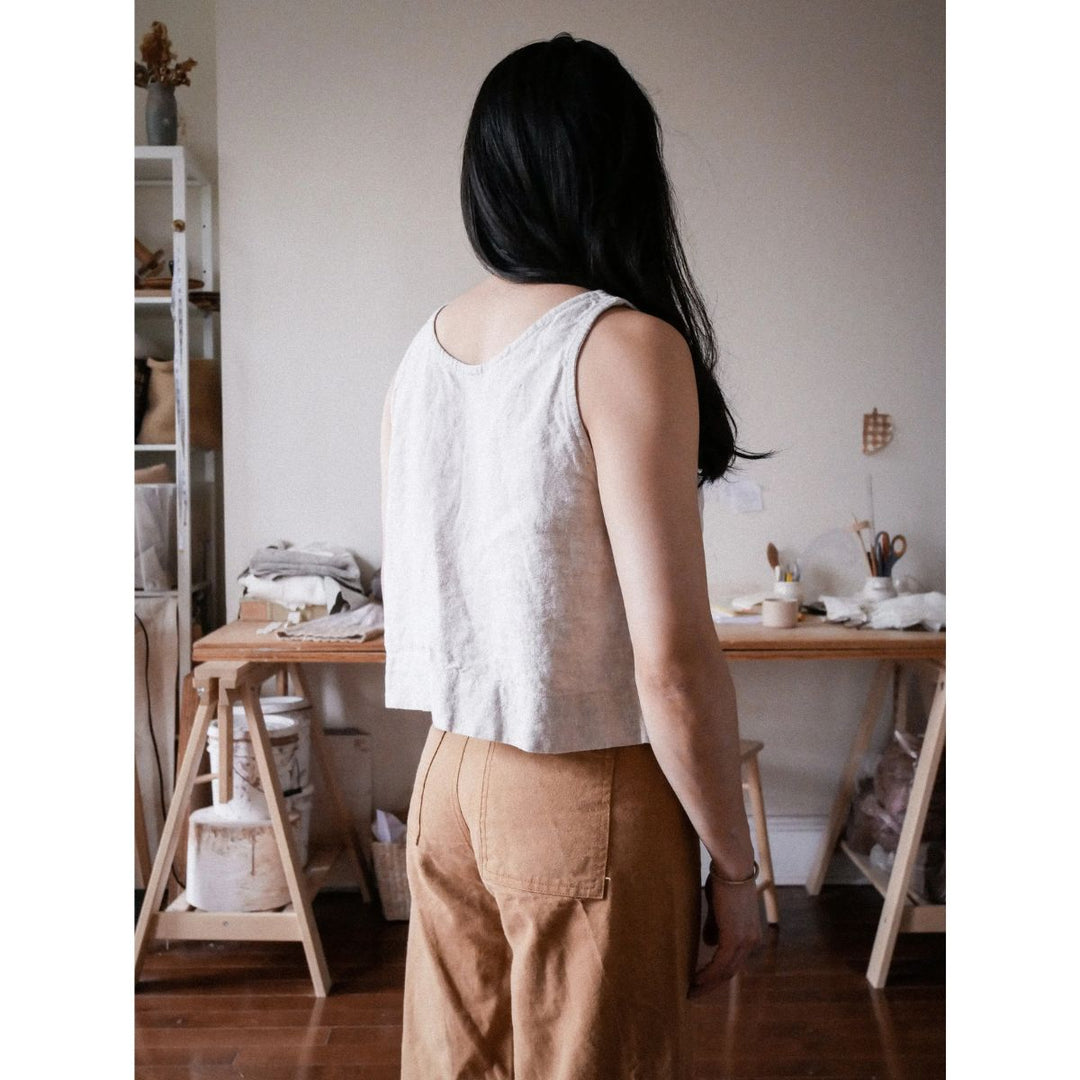 Person wearing a white sleeveless top and brown pants in a room with wooden furniture and shelves.