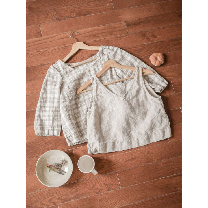 Two hangers with a shirt on a wooden floor next to a cup and plate.