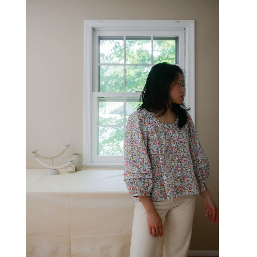 Woman standing in a room with a window and bed in the background