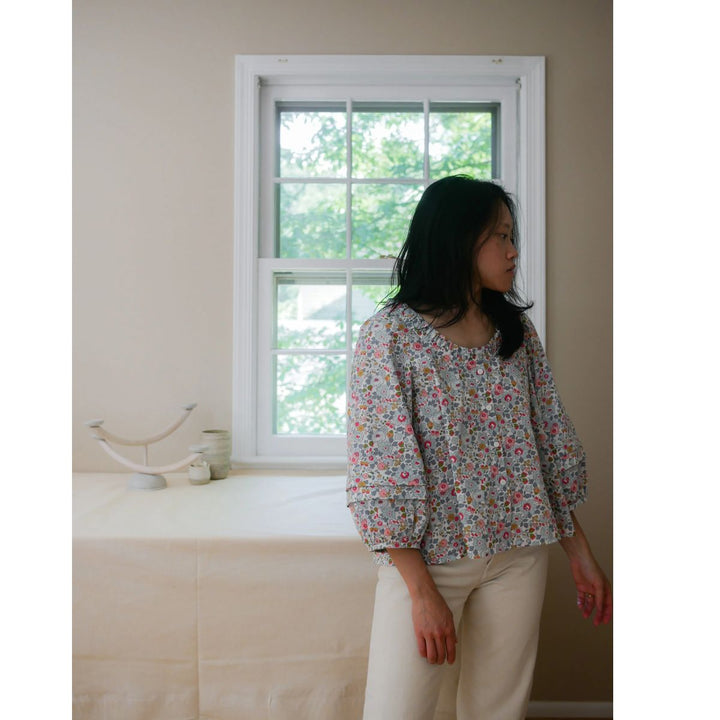 Woman standing in a room with a window and bed in the background