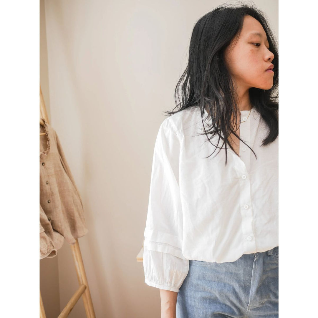 Person wearing a white blouse and blue jeans against a neutral background