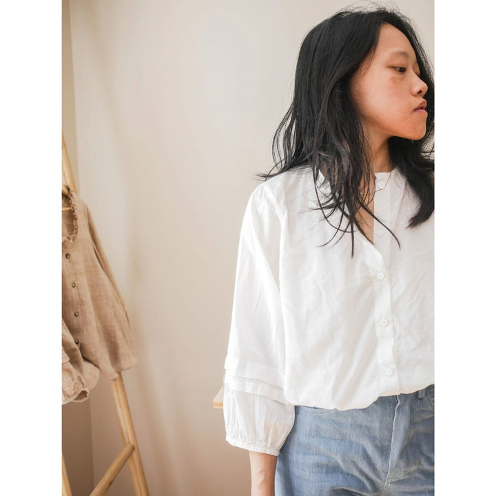 Person wearing a white blouse and blue jeans against a neutral background