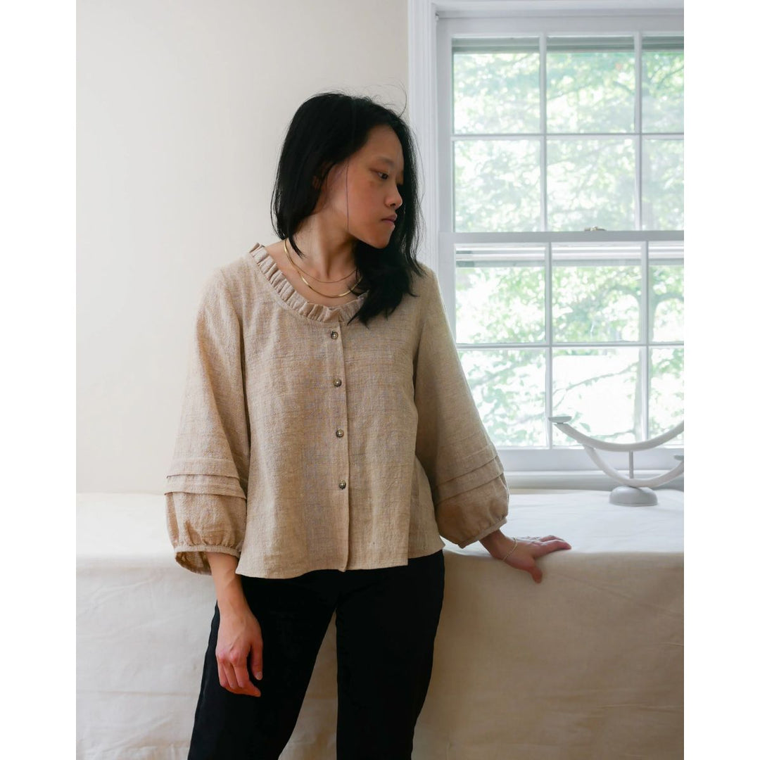 Woman wearing a beige textured shirt in a room with a window and white wall.