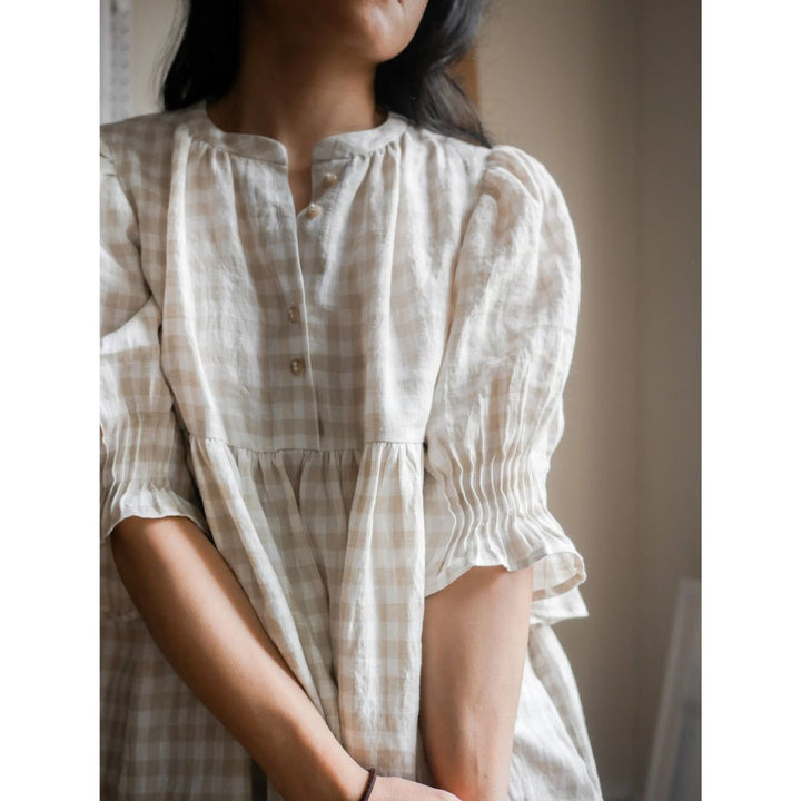 Woman wearing a white checkered dress with puffed sleeves against a neutral background