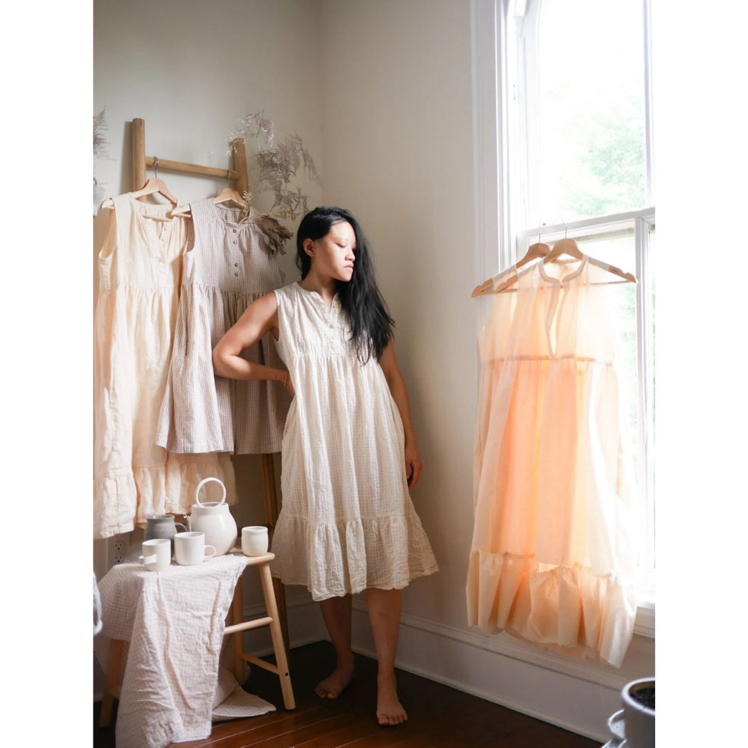 Woman in a white dress standing in a room with hanging dresses and a table.