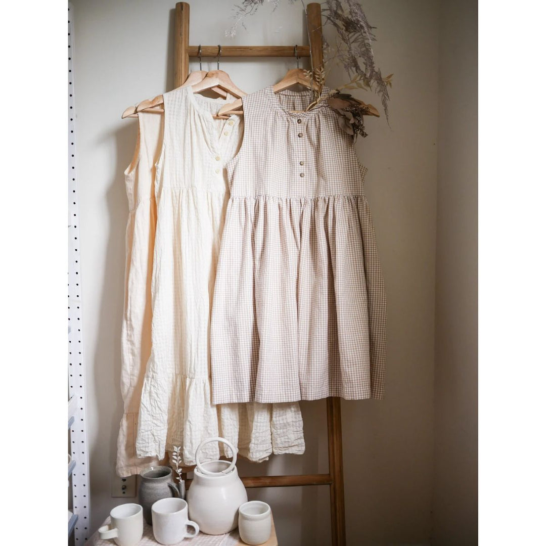 Two dresses hanging on a wooden rack with ceramic items below.