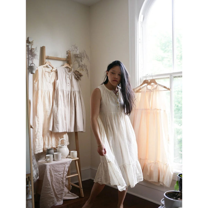 Woman in a white dress standing in a room with light-colored walls and a window.