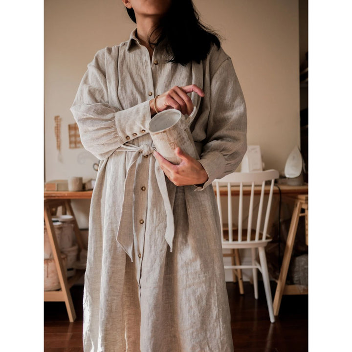 Person wearing a beige linen shirt dress in a home setting