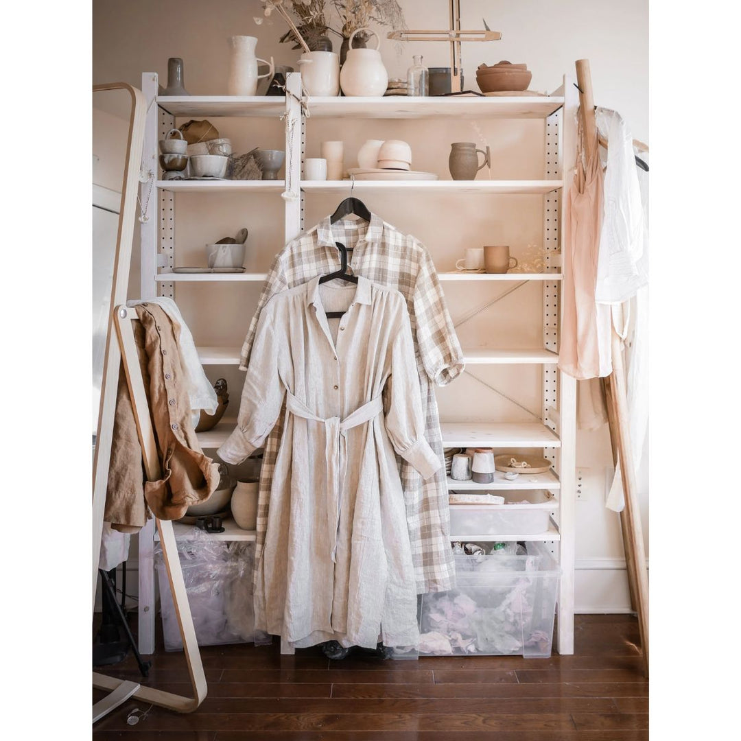 Room with a white shelf displaying various items, including a robe and a coat, with a ladder and wooden floor.
