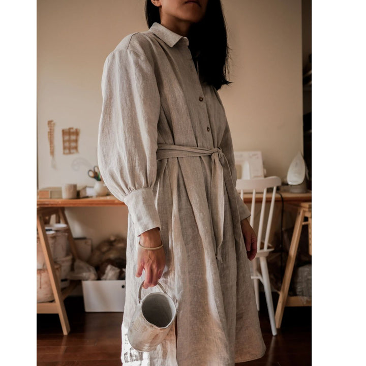 Person wearing a long, light-colored dress holding a small white container indoors.